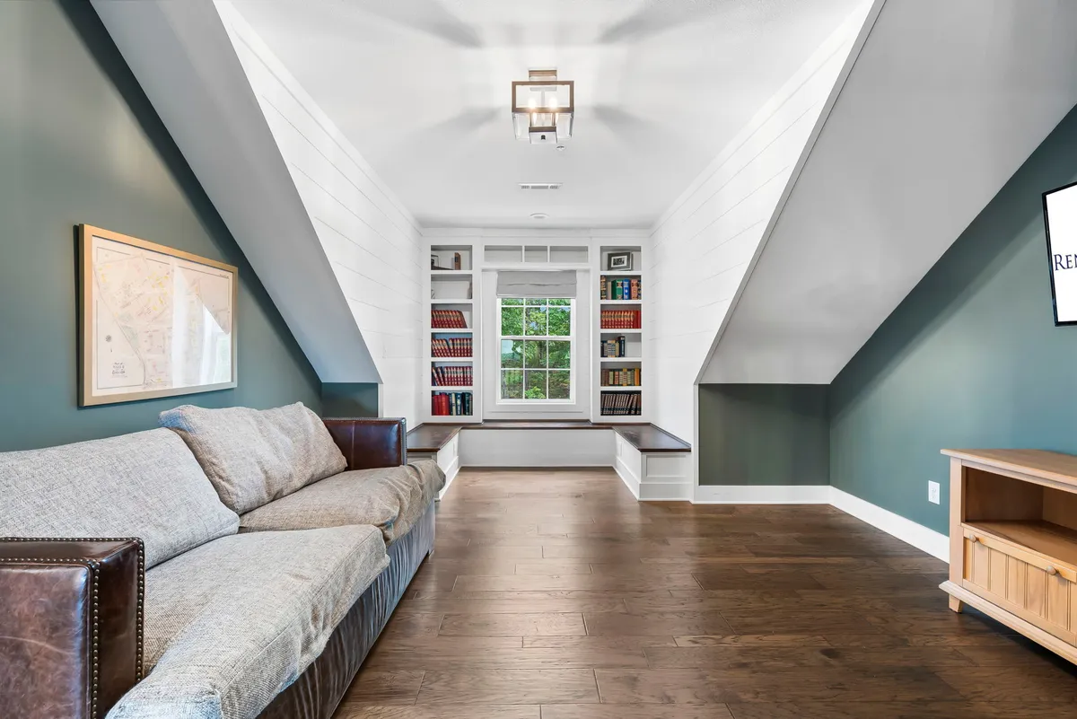 A cozy upstairs library nook featuring a comfortable sofa, built-in bookshelves filled with books, and window seating overlooking the outdoors. The space is intimate and perfect for quiet reading or peaceful reflection.