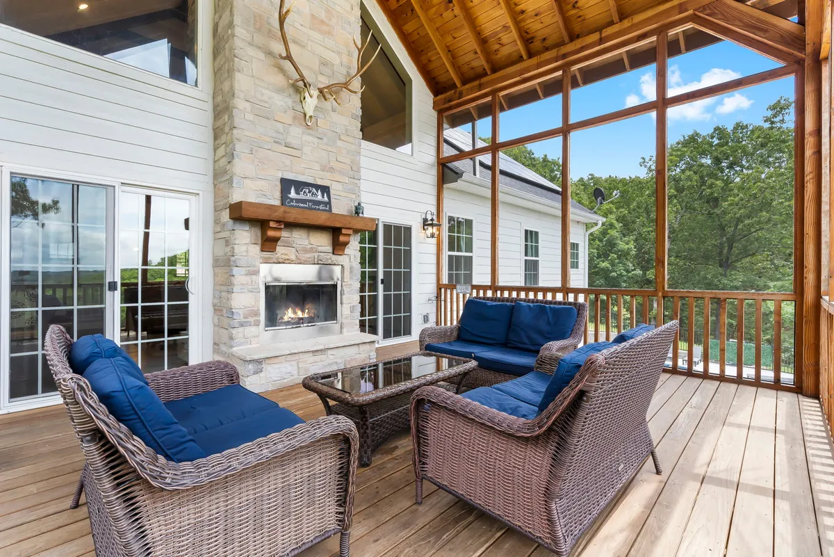 This exterior image showcases a cozy stone fireplace with comfortable seating arranged nearby and large windows looking out onto the landscape. The warm, inviting ambiance is ideal for relaxing with friends or enjoying a drink as the sun sets.