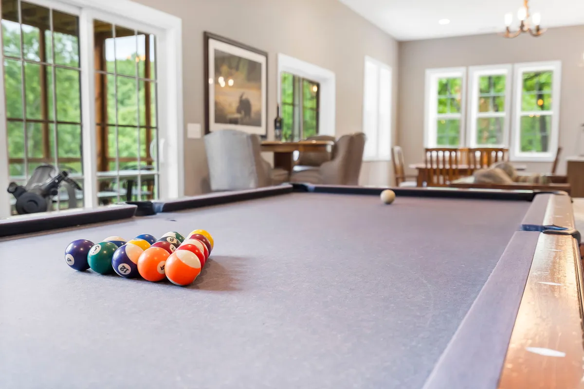 A bright and open game area featuring a pool table, large windows letting in natural light, and adjacent dining space for socializing or card games.