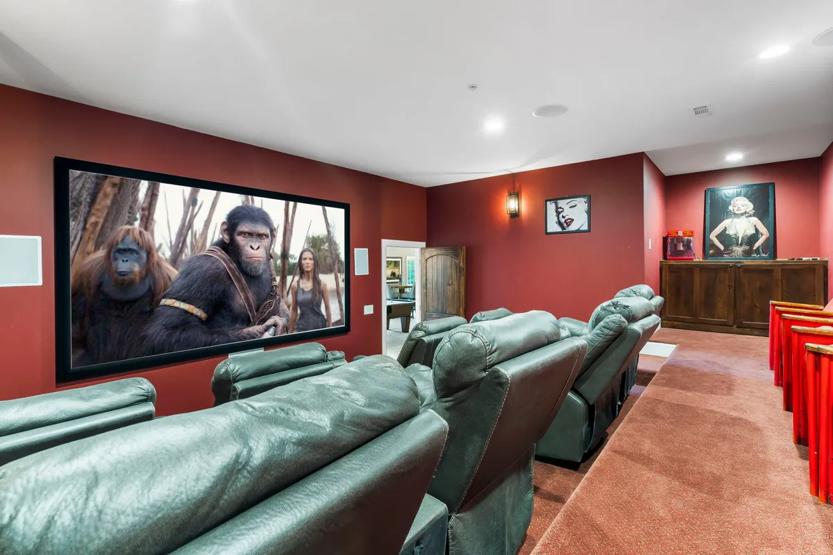 A luxurious home theater with a large screen showing a movie scene, rows of leather recliners, and atmospheric wall art, creating an immersive viewing environment.