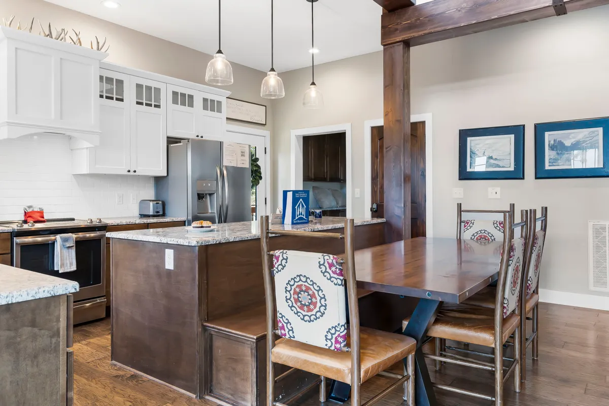 A spacious kitchen with a prominent island and adjacent dining table, illuminated by stylish light fixtures. Ample cabinetry and counter space establish this as a hub for culinary activities, with room for multiple people to cook and dine together.