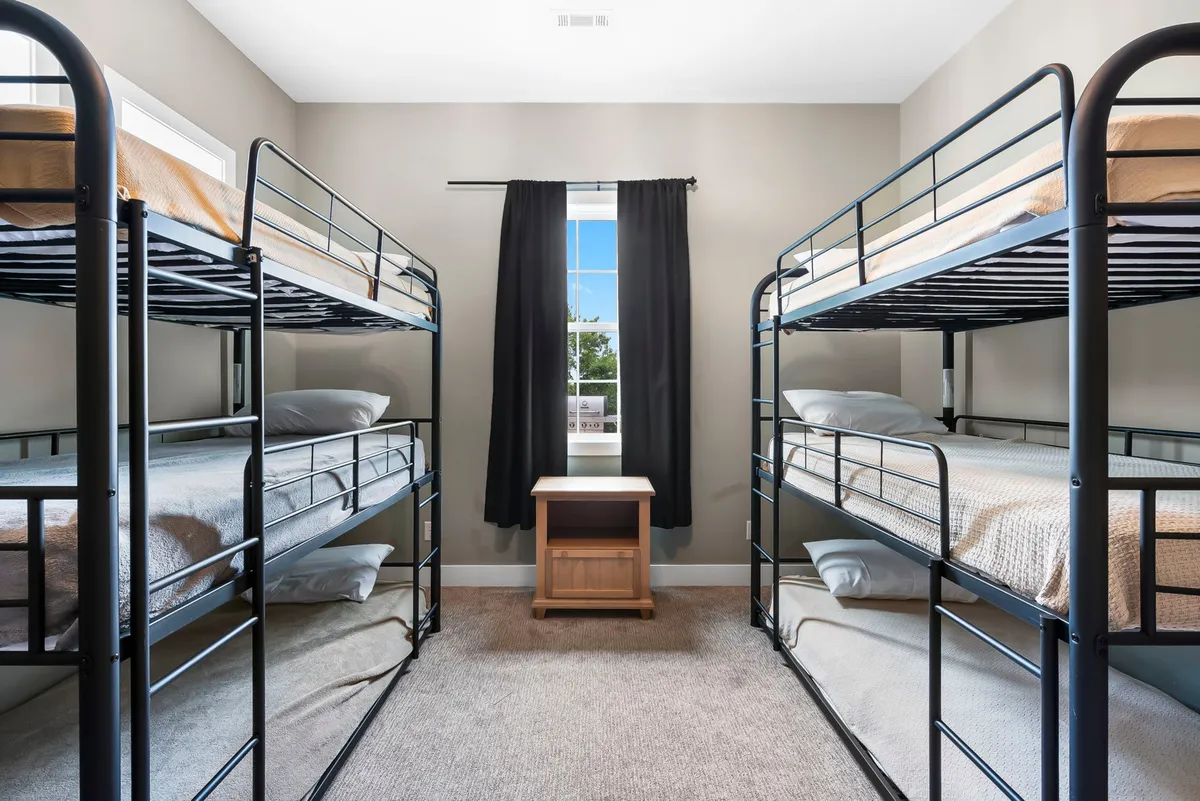 A playful kids’ bunk area with sturdy bunk beds, a window letting in daylight, and a cozy, communal feel. The room is designed for children to share laughter, read, and create memories together.