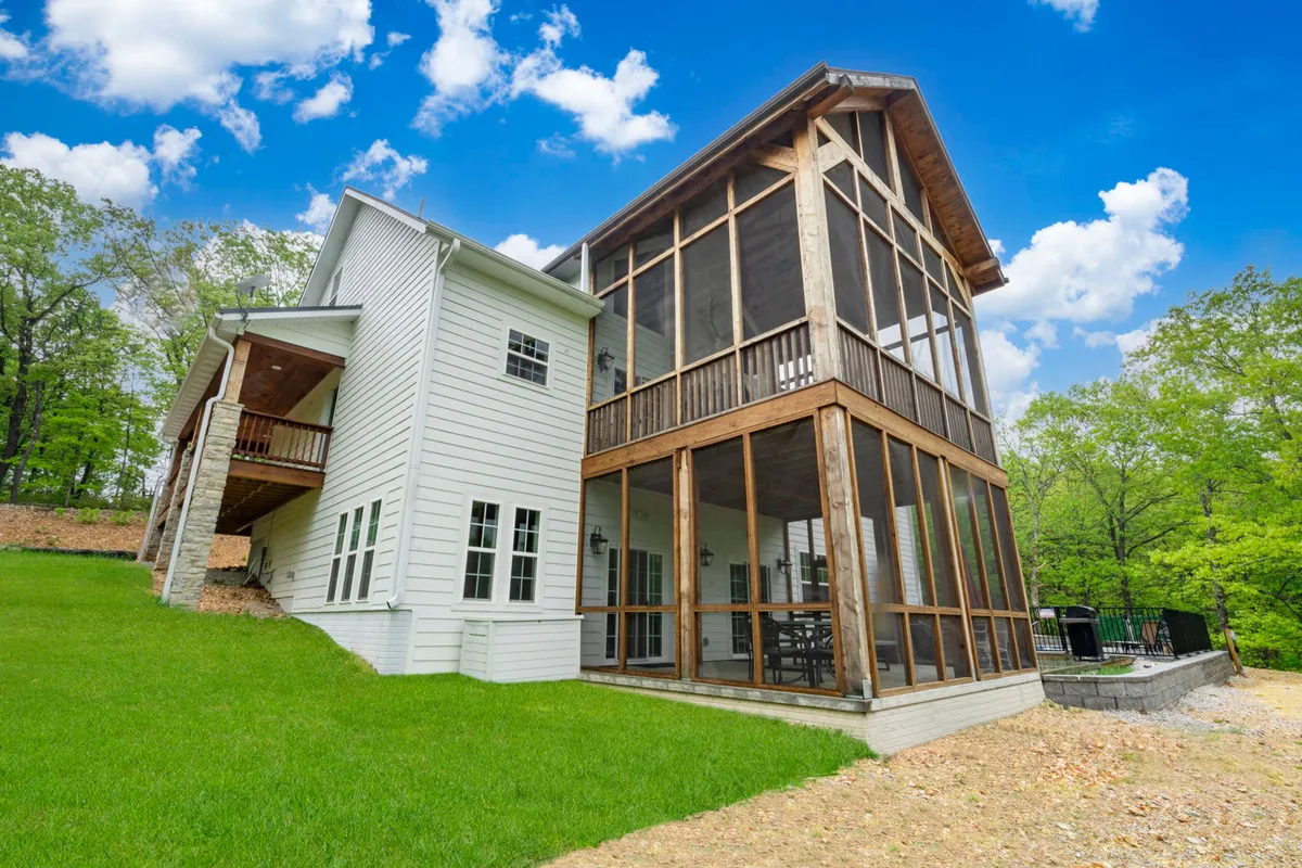 A screened porch overlooks a wide, lush green lawn, bordered by sturdy wooden beams. The scene conveys a serene, natural environment ideal for pets to play safely while their owners relax in comfort on the porch.