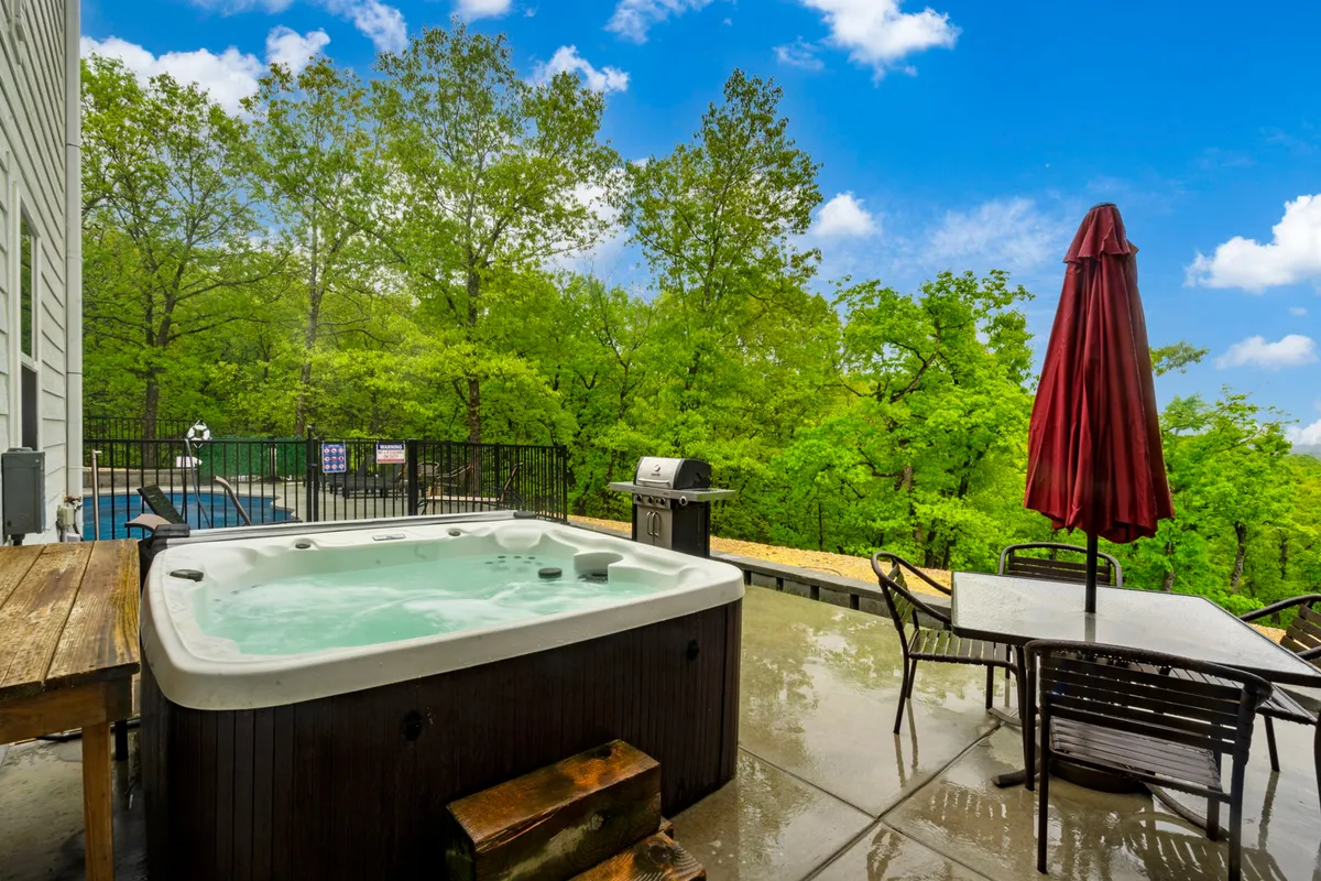 An inviting outdoor space featuring a private hot tub set against lush greenery, an outdoor dining table, and a grill. The hot tub area is tranquil, perfect for sunset or starlit relaxation.
