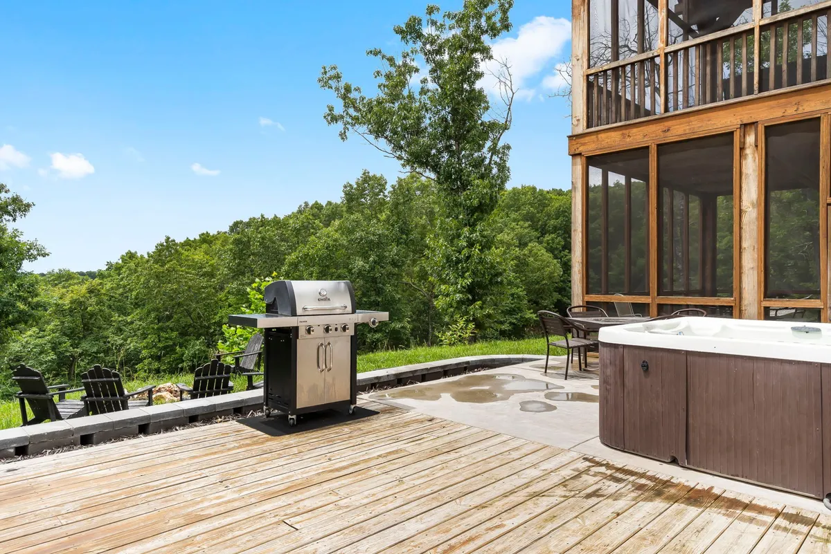 A serene exterior deck scene with a modern grill, hot tub, and tree-lined backdrop. The area is perfect for barbecues, relaxing in the hot tub, and enjoying evening gatherings under the stars.