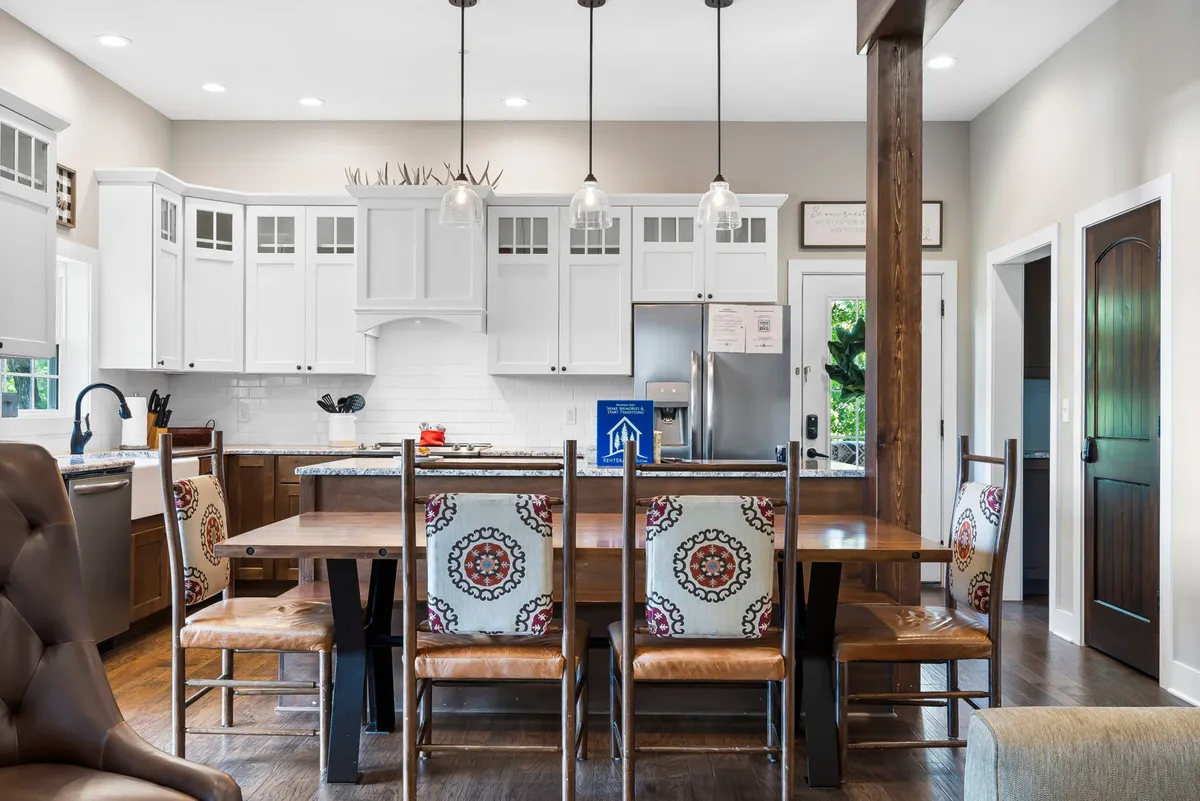 An inviting dining area with a long wooden table, comfortable chairs, and well-lit kitchen cabinets. The setting evokes warmth and togetherness, ideal for hosting dinner parties or sharing meals over lively conversation.