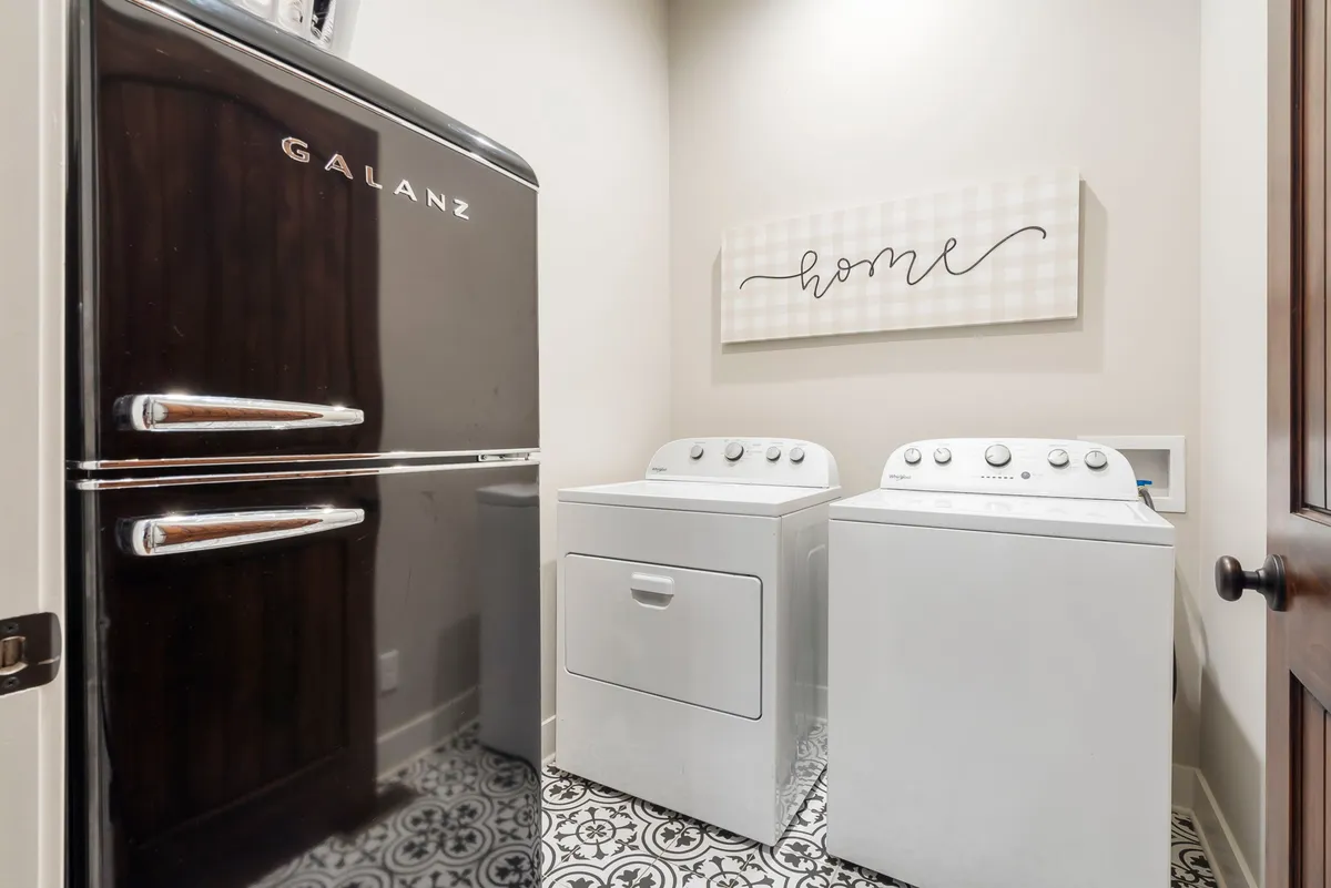 A laundry space featuring a black refrigerator and a washing machine, accented with homey décor. The addition of a refrigerator here underlines the home's ample food storage capabilities.